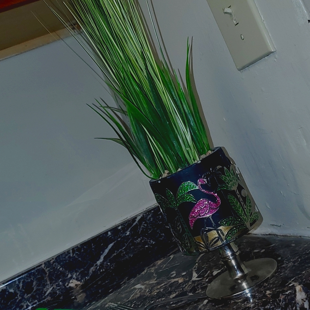 A flamingo and palm tree candle holder or plant holder with a grass plant inside